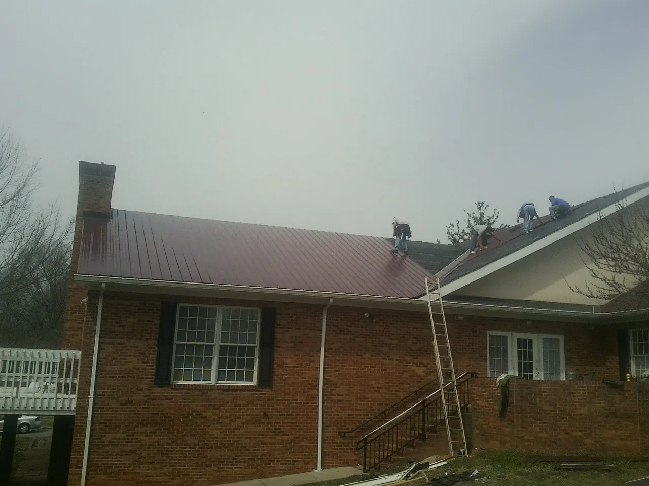 Crew setting red metal roofing panels on a brick home in Medford