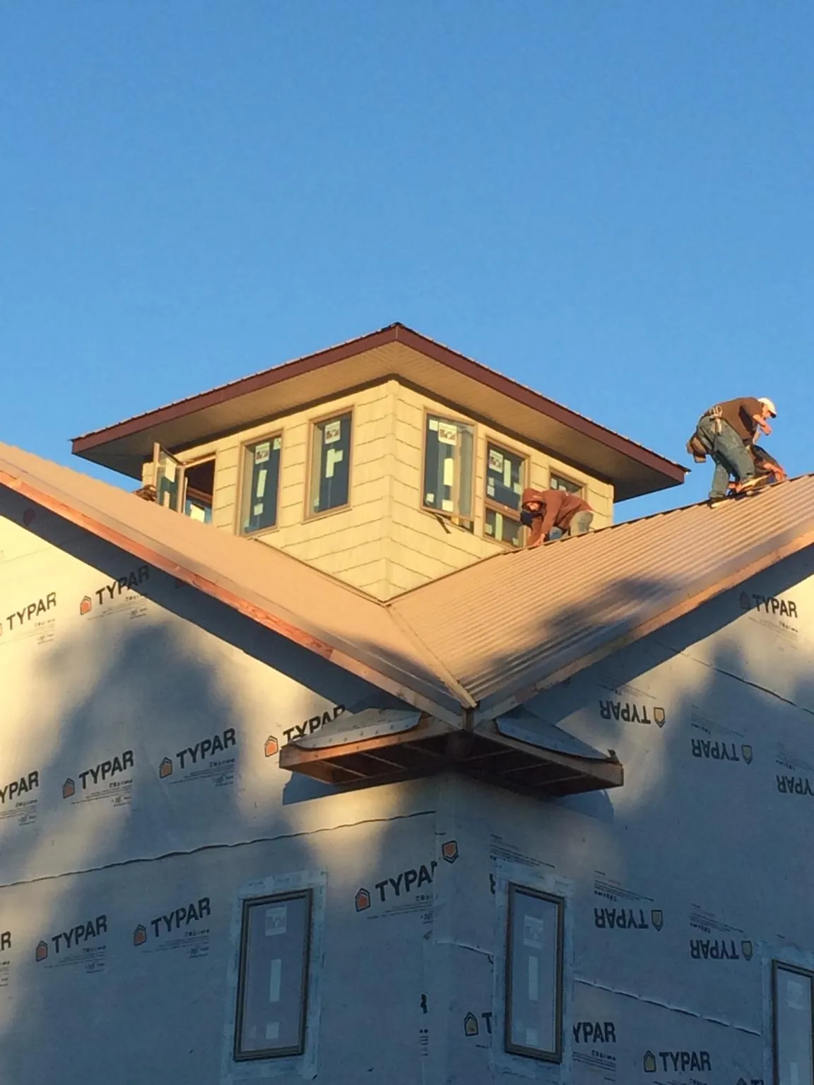Roofers working around a rooftop cupola on a new metal roof at sunset — Roof Waterproofing in Medford by Roofing Brothers